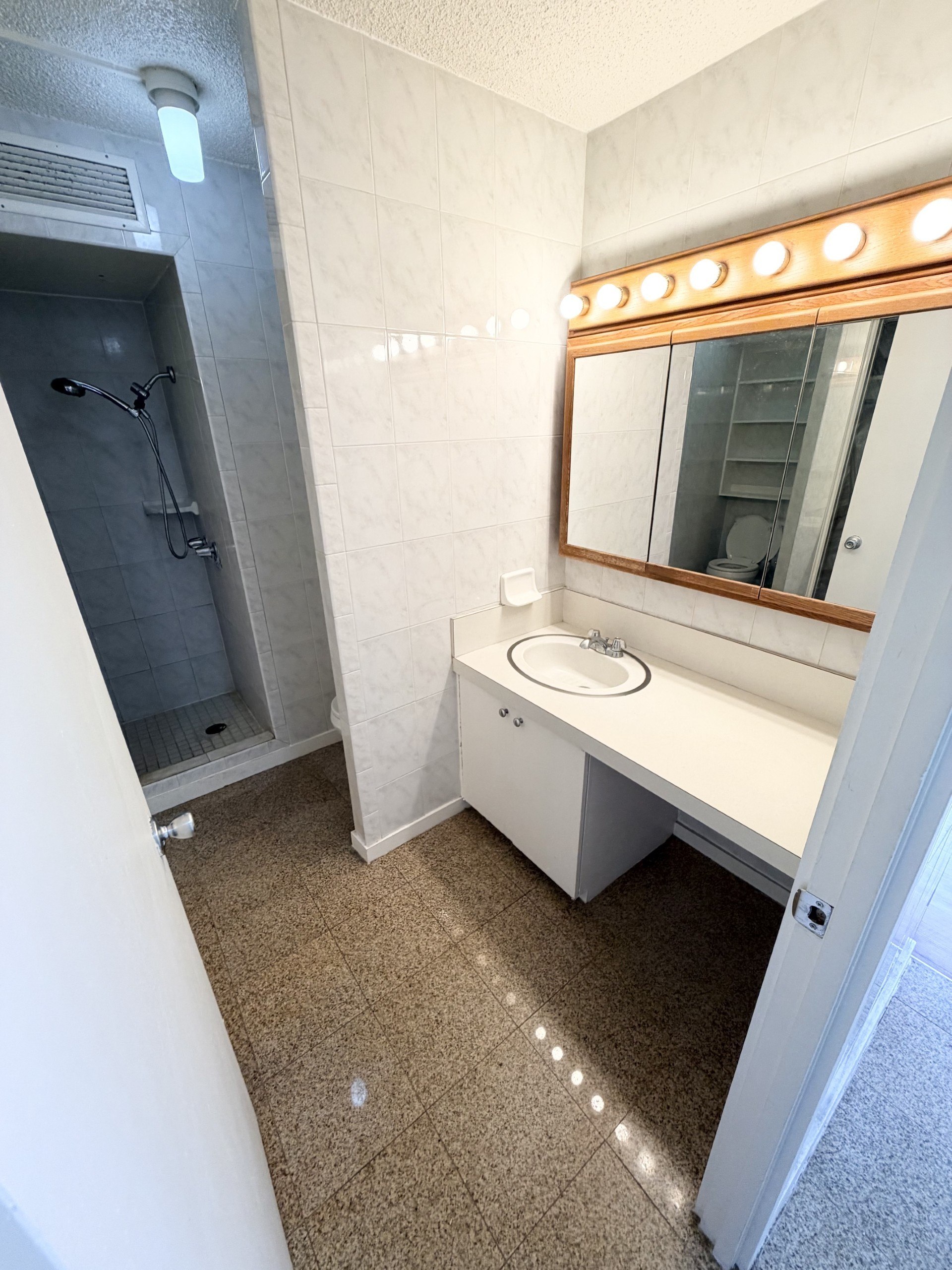 A bathroom with a white vanity and a mirror with lights around it.